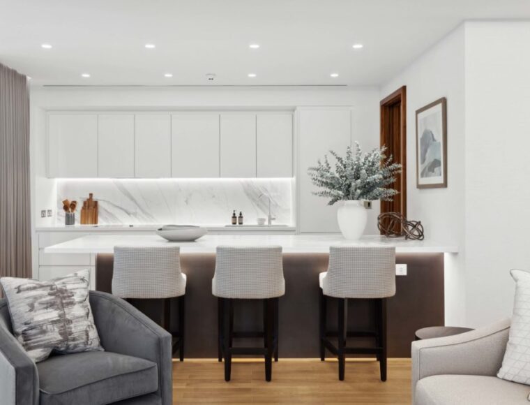 Open plan kitchen and lounge decorated in white, furnished with an armchair and bar stools