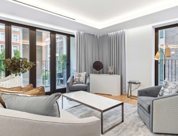 Lounge room surrounded by large balcony windows, and furnished with grey sofa's and mirror table.