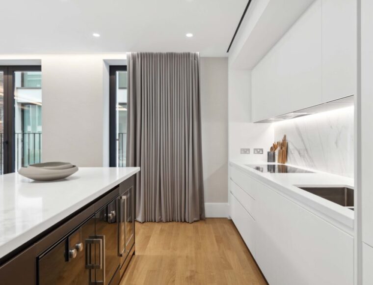 A straight view of the kitchen, showcasing the white kitchen counters and long balcony curtains.