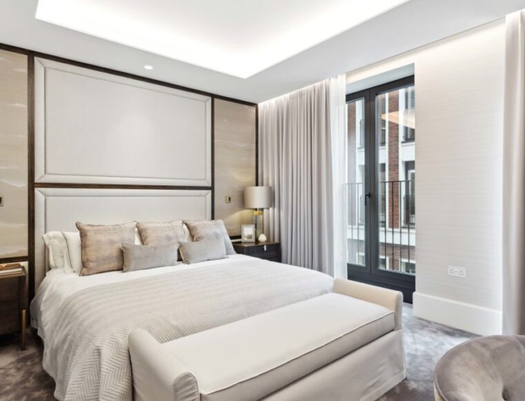 A bedroom with a balcony, double bed and dark brown side-tables against a cream theme wall.