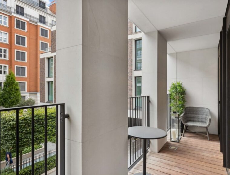 A gated balcony with wooden floors, an arm and chair and tall coffee table.